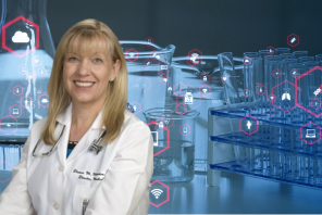 Dr. Milewicz is wearing a lab coat and is standing in front of a background of medical research items like test tubes and beakers